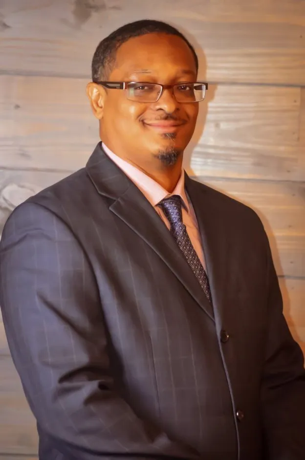 Dion Fletcher, President, in a suit and tie in front of a wooden wall