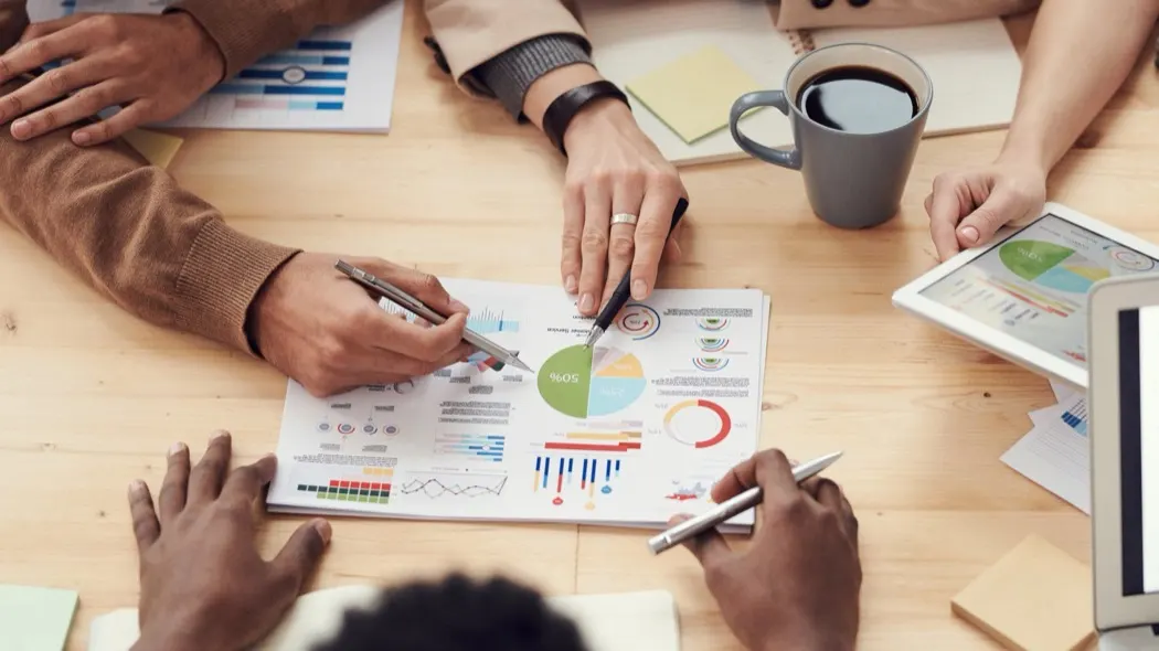 Hands pointing at a printed chart with pie graphs on a wooden table