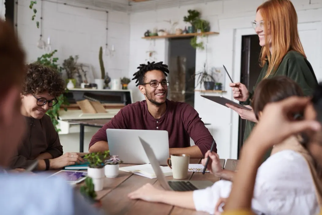 Group of coworkers laughing together around a table with a laptop