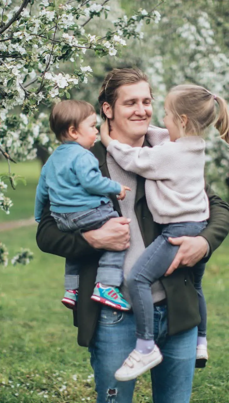 Smiling father holding a toddler and a young girl under a flowering tree