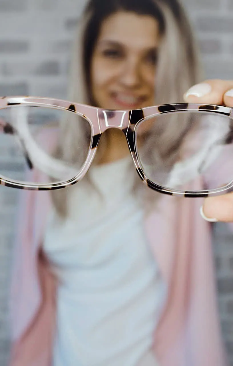 Woman holding up a pair of pink-framed eyeglasses toward the camera