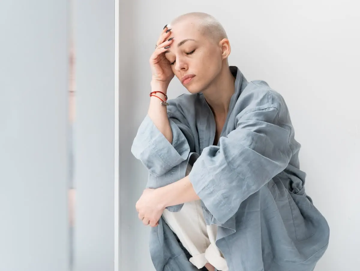 Woman in a gray robe sitting on a window ledge with her head resting on her hand