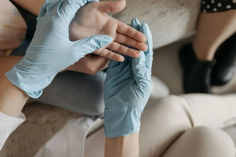 Hands in blue medical gloves holding a patient's hand