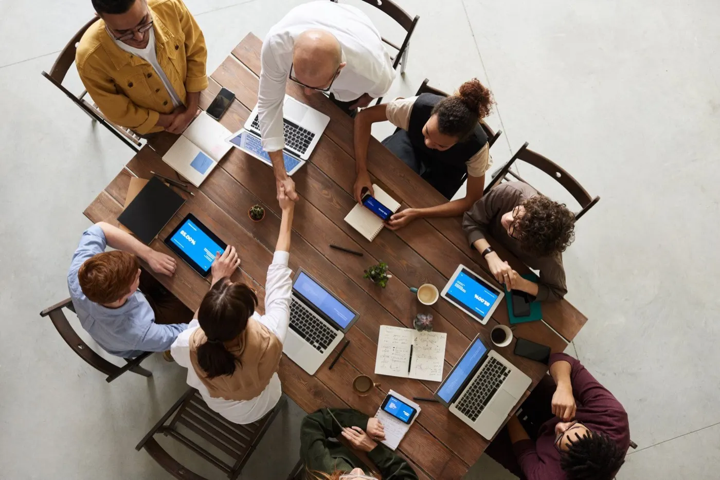 Overhead view of colleagues shaking hands at a wooden table with laptops
