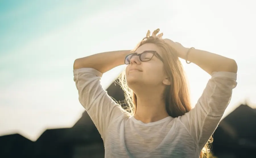 Woman with glasses tilting her head back in warm sunlight
