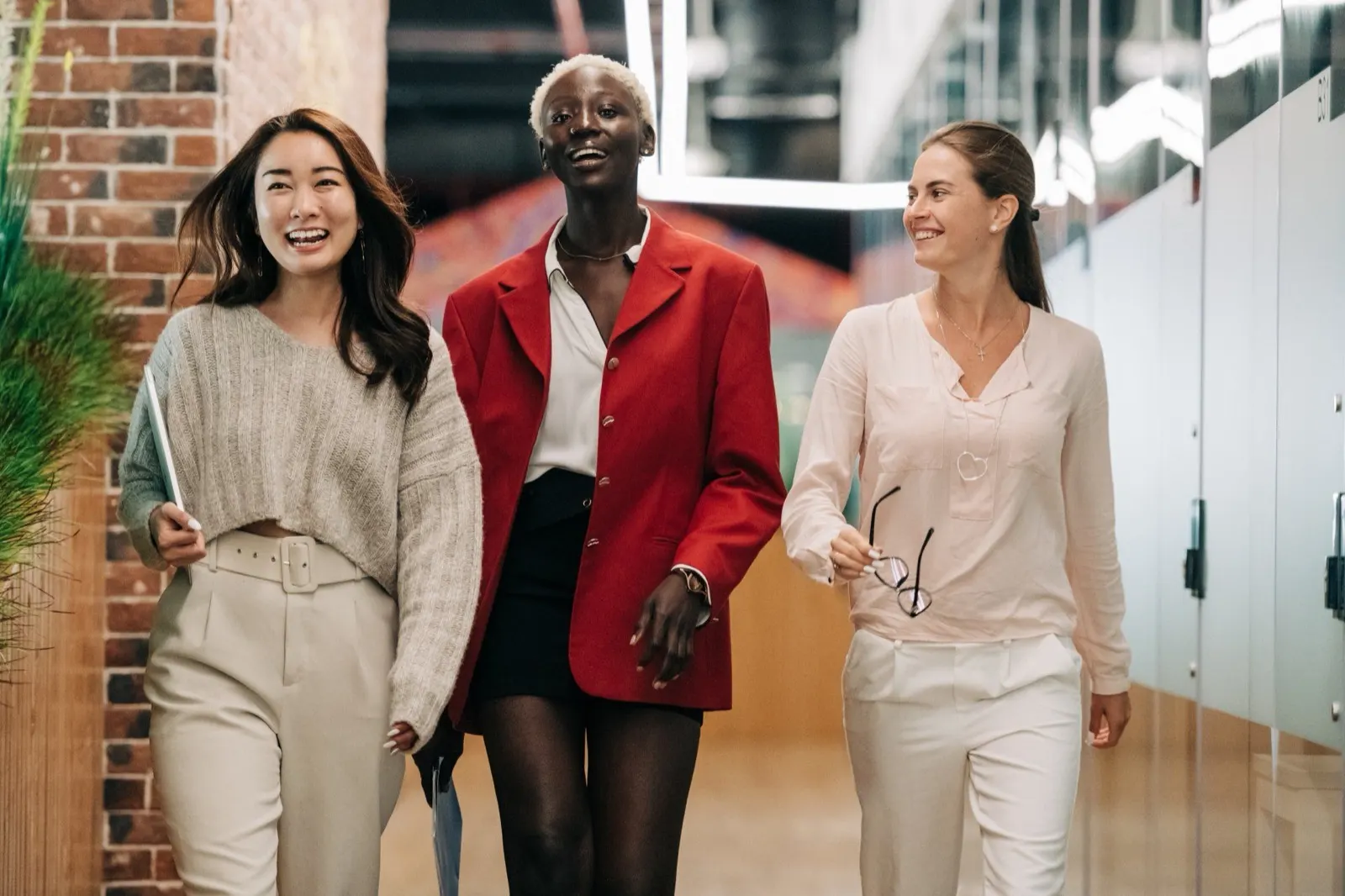 Three smiling businesswomen walking together through an office hallway