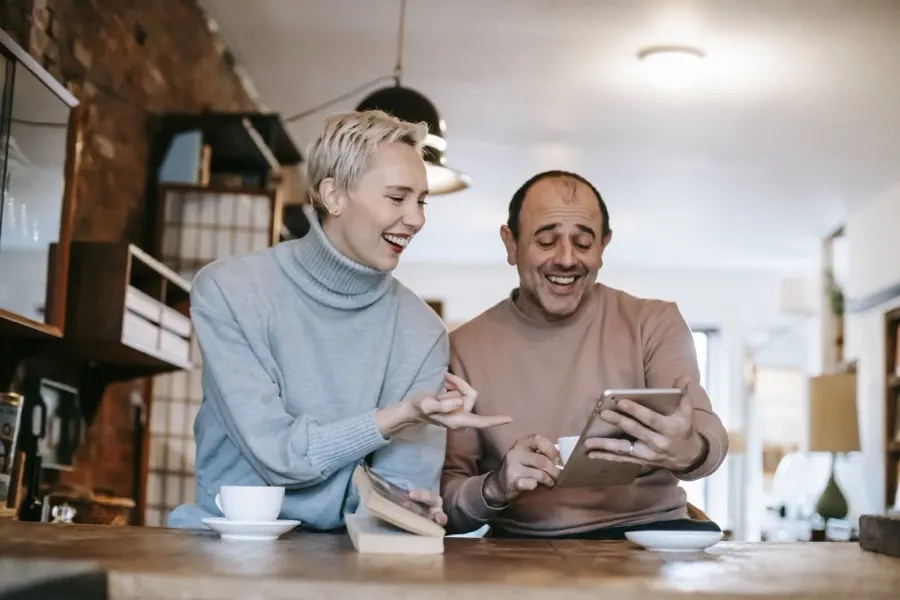 Two coworkers smiling at a tablet over coffee