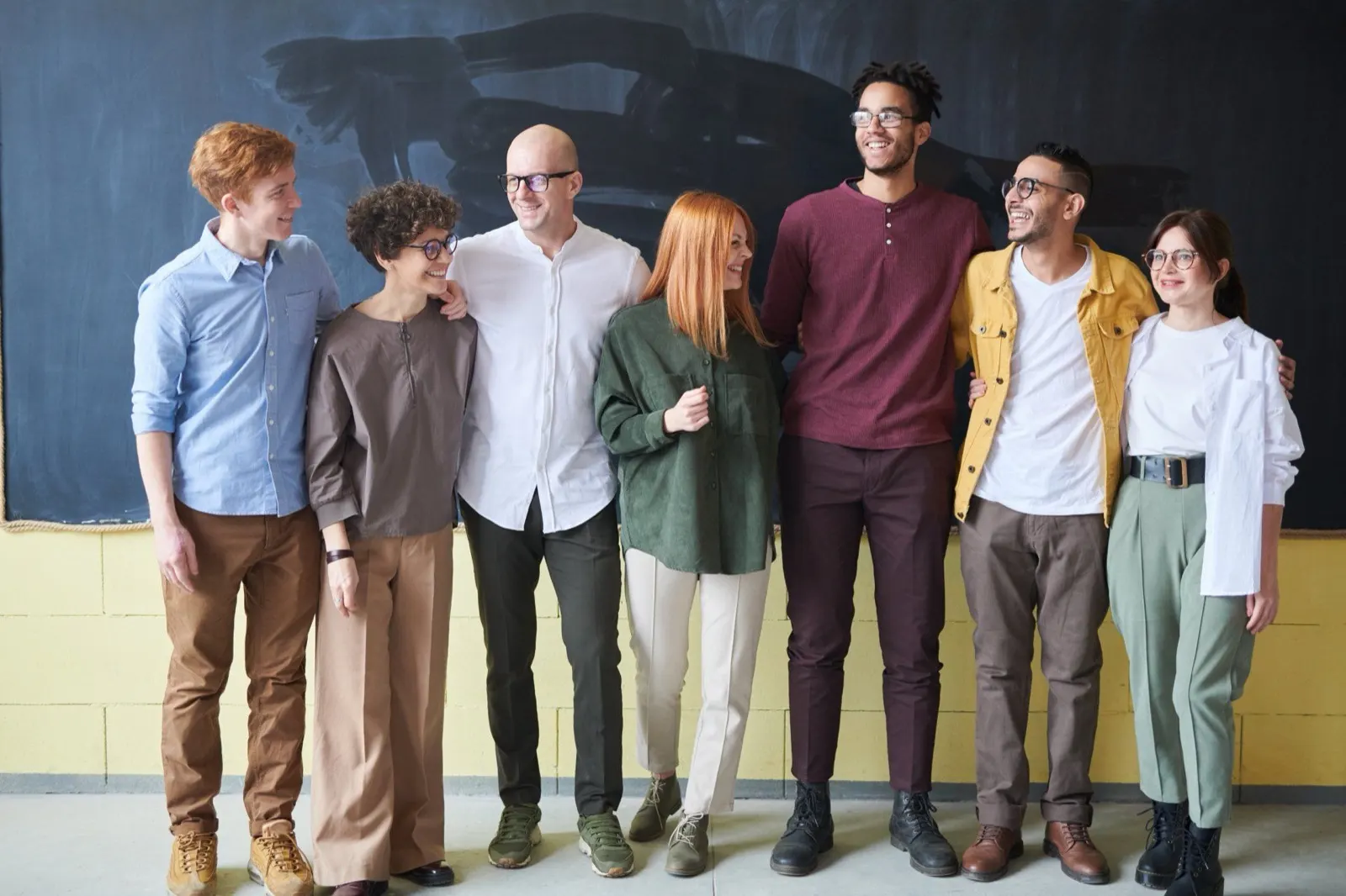 Seven coworkers standing together arm in arm in front of a chalkboard