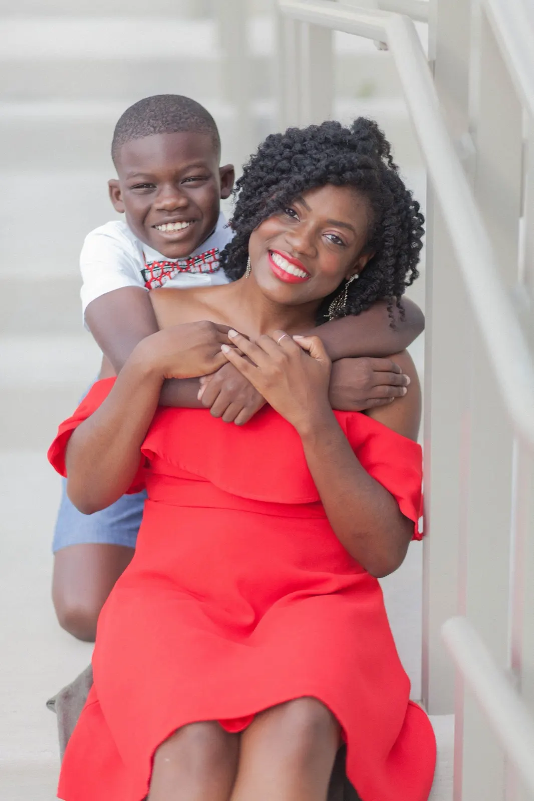 Smiling mother in a red dress hugged from behind by her young son