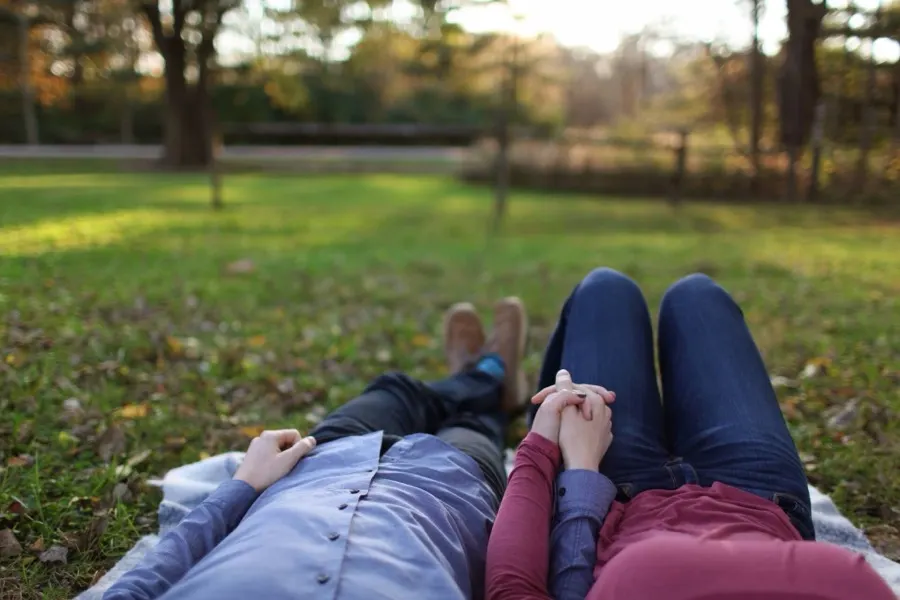 Couple lying on a blanket in a park holding hands