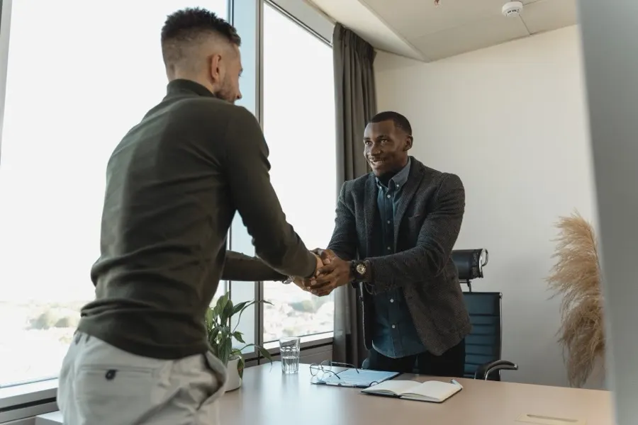 Two men in business clothes shaking hands in a sunlit office